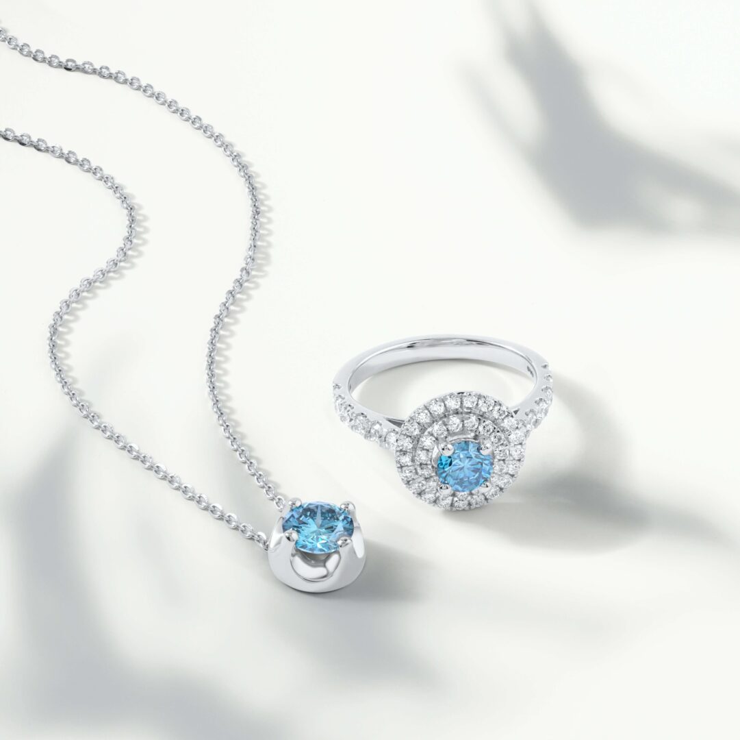 A blue diamond necklace and ring on top of white surface.