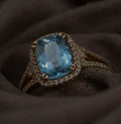 A blue diamond ring is sitting on top of a brown cloth.